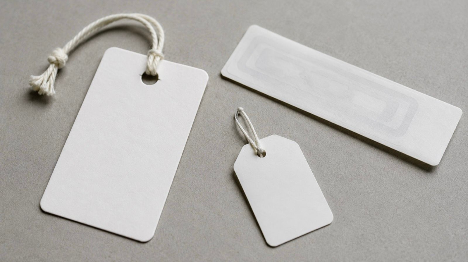 Three blank RFID label formats on a gray surface: an apparel hangtag, an adhesive label with a visible RFID inlay antenna, and a small jewelry tag
