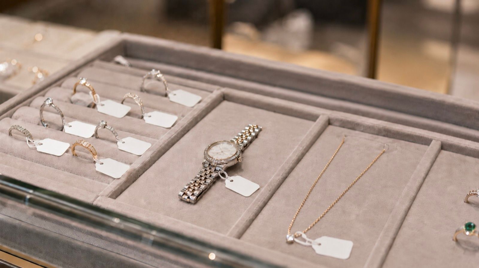 A jewelry display tray of rings, a watch, and a chain, each piece carrying a small blank RFID jewelry tag